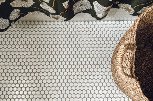 white penny tiled floor with gray grout below a green flowered shower curtain and laundry basket